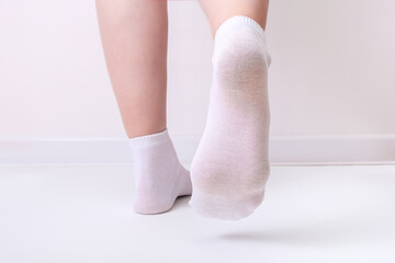 Woman female legs wearing white plain cotton socks of classic style with elastic band standing against white background and showing foot underside, sole