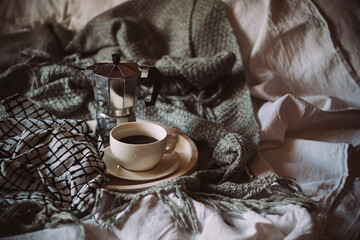 Cup of coffee on tray in cozy winter bad with wool blanket