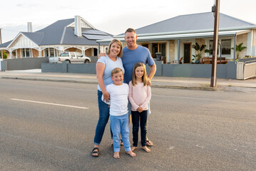 portrait of Happy family of four embracing and smiling in front of new dream home.