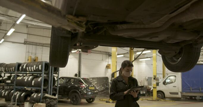 Female car mechanic inspecting vehicle using digital tablet in workshop