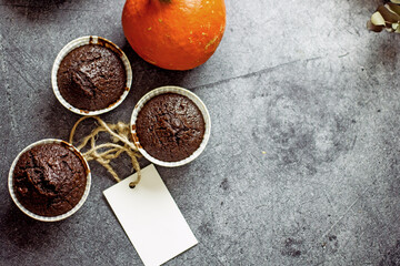 Gluten-free pumpkin chocolate muffins on a gray plate surrounded by ingredients, next to a white card for the inscription. Copy space, flat lei. Healthy baking concept
