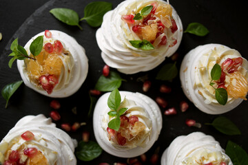 dessert called Anna Pavlova. Meringue with cream garnished with pomegranate, tangerine slices and Basil leaves