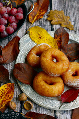 Close-up of fried donuts on plates, grapes, walnuts and colorful autumn leaves on a rustic wooden background.