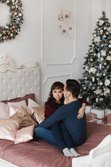 Sweet couple hugging on the bed in a bedroom decorated for Christmas holidays