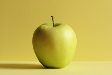 Single green apple on a yellow horizontal background. Minimalism concept.