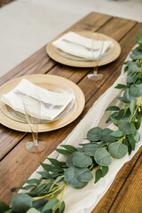Gold and White Place Settings for Wedding Reception Placed on a Wooden Sweetheart Table with Greenery Vine