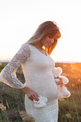 Young happy pregnant woman in white dress on sunset - 389734819