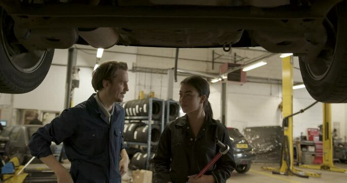 Car mechanic and trainee looking at car in auto repair workshop