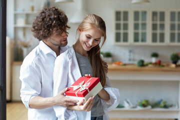 Handsome young man giving present to beautiful woman at home. Happy family.