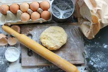 Hands kneading dough. Ball of dough on a rustic wooden background with dusting of flour. Dough with flour near broken egg with yolk in bowl and other utensil, ingredients lies on dark concrete table. 