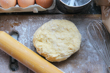 Hands kneading dough. Ball of dough on a rustic wooden background with dusting of flour. Dough with flour near broken egg with yolk in bowl and other utensil, ingredients lies on dark concrete table. 