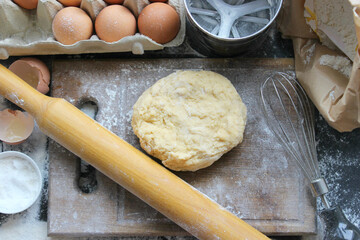 Hands kneading dough. Ball of dough on a rustic wooden background with dusting of flour. Dough with flour near broken egg with yolk in bowl and other utensil, ingredients lies on dark concrete table. 