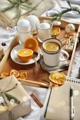 Cosy home flat lay composition with present boxes, blank copybook, a pen, tea and cones on a bed. Holiday shopping list, wish list or New Year Goals concept, presents checklist. Selective focus