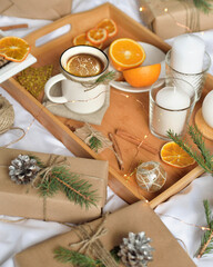 Cosy home flat lay composition with present boxes, blank copybook, a pen, tea and cones on a bed. Holiday shopping list, wish list or New Year Goals concept, presents checklist. Selective focus