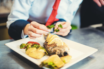 Chef cook in a fancy restaurant kitchen finishing a dish with care