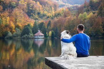 man and dog sitting by autumn lake social distancing