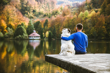 man and dog sitting by autumn lake social distancing