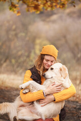 Young woman hugs golden retriever on background of autumn forest