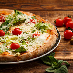 Caesar pizza with salad and tomatoes on wooden background