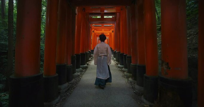 Tracking shot, Japanese woman walks through Torri gates in Fushimi Inari Taisha