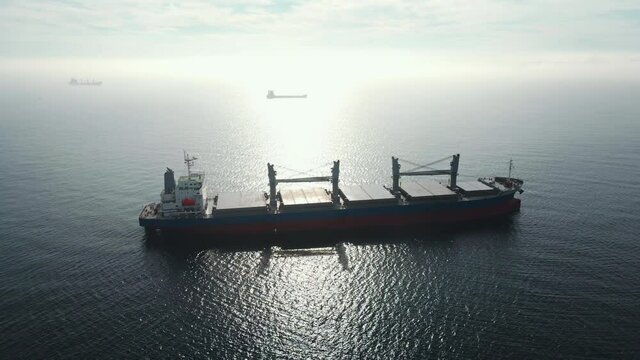 Aerial view bulk carrier docked of cargo ship, transports containers with goods, by sea sunset summer. Arrival of merchant ship in city seaport with crane