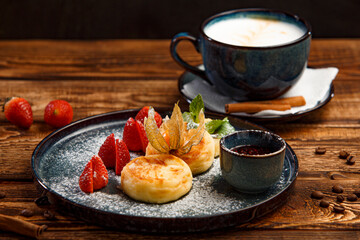 cheesecakes with jam, strawberries and powdered sugar with cappuccino on a wooden background