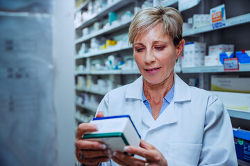 Caucasian senior female pharmacist checking labels on medication prescriptions standing in pharmacy drugstore 