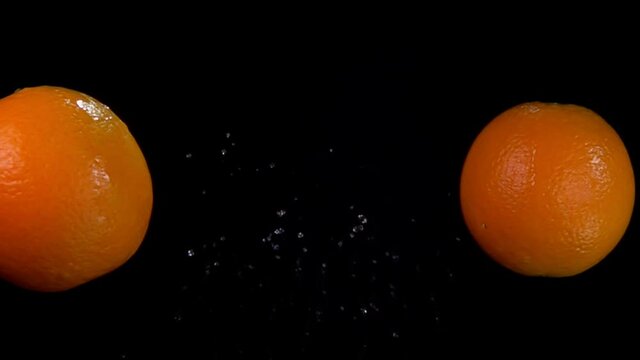Two ripe juicy oranges are flying and colliding with each other rising drops of water on the black background in slow motion