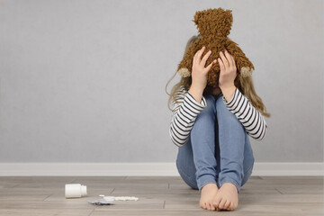Psychological, mental health. A teenage girl sits on the floor and covers her face with a teddy...