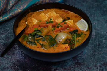 Vegan thai red curry with carrot, tofu and bock choy in black bowl, copy space