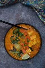 Vegan thai red curry with carrot, tofu and bock choy in black bowl, copy space