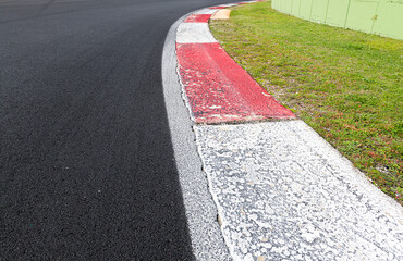 Obraz premium Close up of rough curb at right turn on motor sport track with green field and black asphalt
