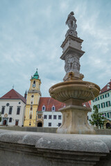 Fototapeta premium Maximilian fountain in Bratislava, Slovakia on the main Square of the city, with town hall seen in the background on a gray dull day.