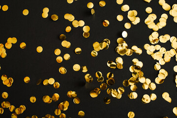 Golden confetti on black background. Festive holiday backdrop. Birthday congratulations Christmas New Year. Flat lay, top view, copy space.