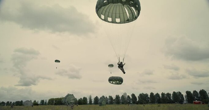 Man watches soldiers parachute over Normandy field, low angle