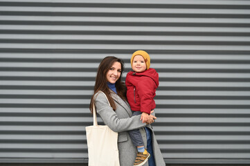 Mom with a baby in her arms in warm clothes, on a gray background