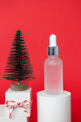 Skincare serum bottle stay on cylinder podium and gift box, Christmas tree decor on red background, vertical.