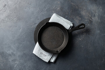 Small cast iron pan with a blue linen napkin on a dark concrete background, place for text