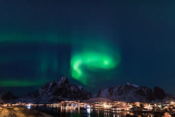 Dancing green polar lights over the village Reine on the Lofoten islands in Norway at night in winter with snow capped mountains