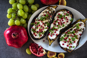 Grilled eggplants with yogurt sauce and pomegranate seeds on grey table. Top view photo of fresh made vegetarian meal. 