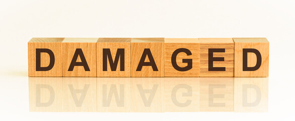 Wooden Blocks with the text: DAMAGED. The text is written in black letters and is reflected in the mirror surface of the table.