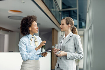 African American businesswoman and her female colleague talking in a hallway.