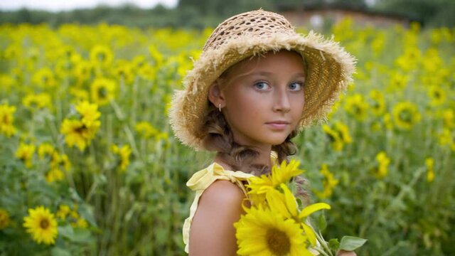 Girl holding bouquet of sunflowers and rotating on field. Adorable happy teenage girl in wicker hat having fun on sunflower field in countryside
