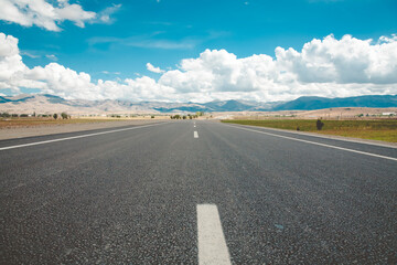 Asphalt road through yellow field and clouds on blue sky on summer day