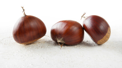 Three chestnuts isolated on a white painted wooden background.