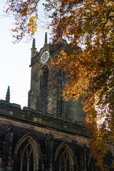 Fototapeta na wymiar Church tower of St Mary The Virgin Church in the city centre of Barnsley in England, UK. Christian prayer house. Religious building. Autumnal tree in the frame. Select focus.