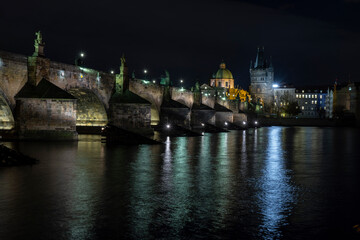 
illuminated stone monument of karluv bridge from 14 century on river vltava and light from street lighting in the center of prague and prague architecture around