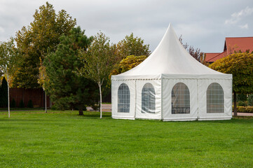 a white outdoor pavilion a on a green mowed lawn in the middle of the park