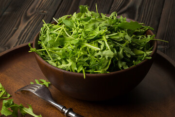 Fresh rucola (Eruca sativa) in a bowl on a dark wooden table.