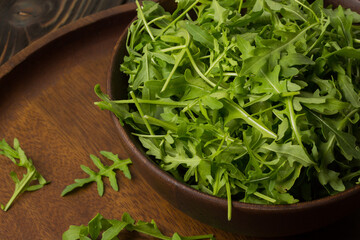 Fresh rucola (Eruca sativa) in a bowl on a dark wooden table.
